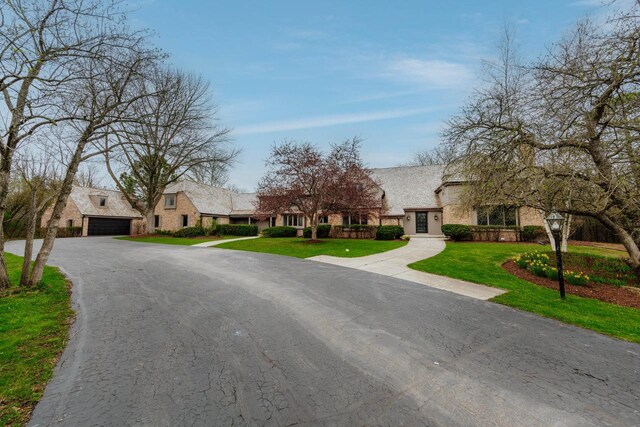 view of front of home with stone siding, a front yard, a garage, and asphalt driveway