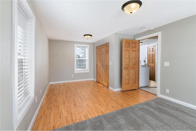 unfurnished bedroom with washer / dryer, a closet, wood finished floors, and baseboards
