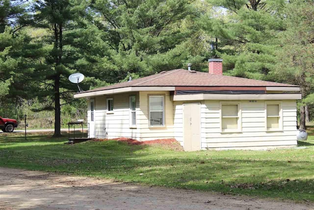 view of front of property featuring a chimney, a shingled roof, and a front lawn