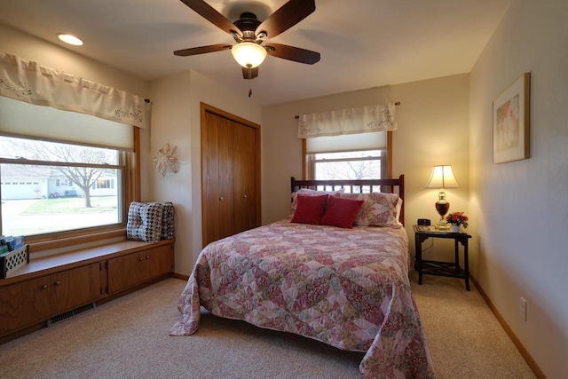 bedroom with a closet, light colored carpet, visible vents, ceiling fan, and baseboards