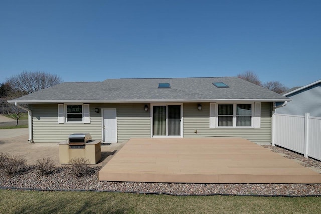 rear view of house featuring roof with shingles and fence