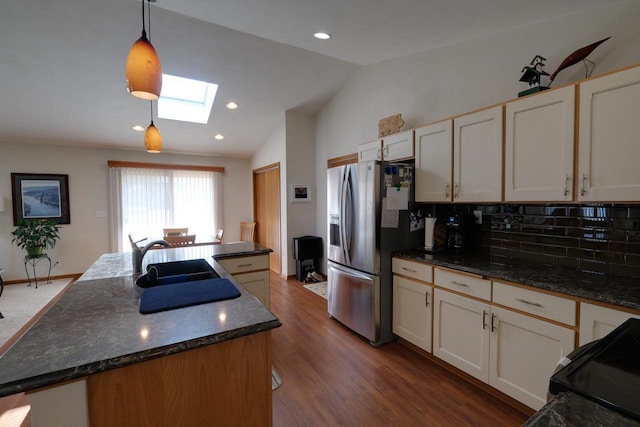 kitchen with stainless steel fridge, lofted ceiling with skylight, a sink, a kitchen island with sink, and decorative light fixtures