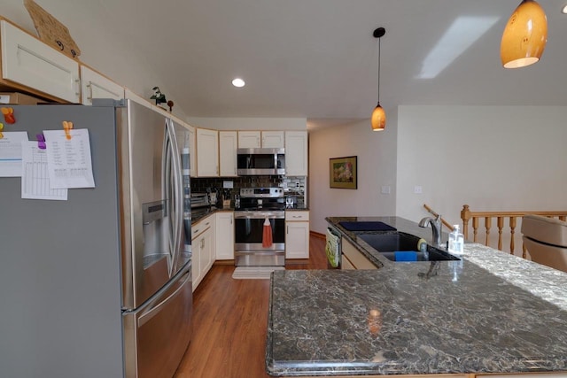 kitchen with a sink, stainless steel appliances, tasteful backsplash, wood finished floors, and hanging light fixtures
