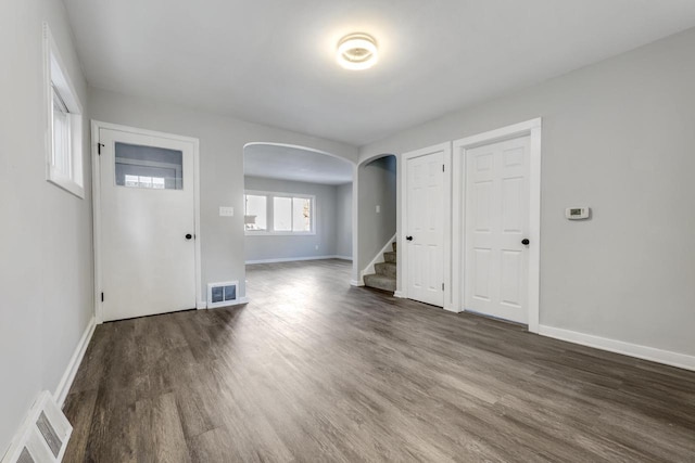 empty room featuring baseboards, visible vents, stairs, wood finished floors, and arched walkways