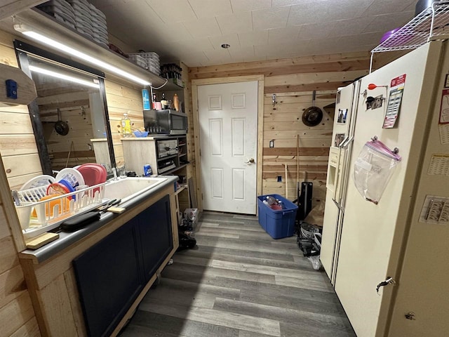 interior space with stainless steel microwave, wooden walls, white fridge with ice dispenser, and wood finished floors