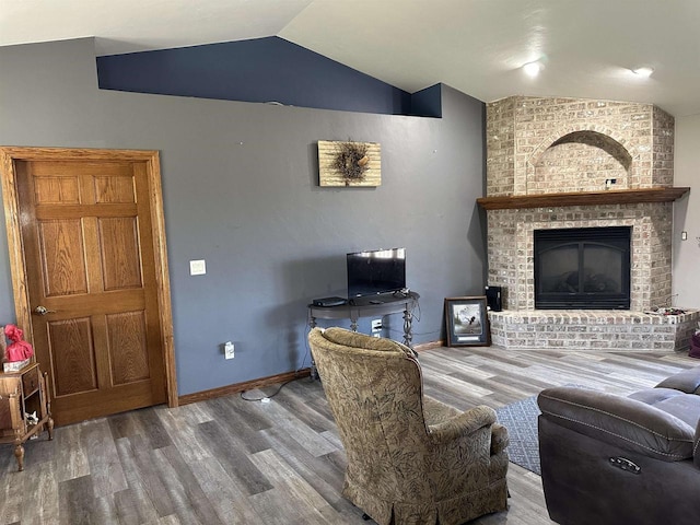 living room featuring vaulted ceiling, a fireplace, baseboards, and wood finished floors