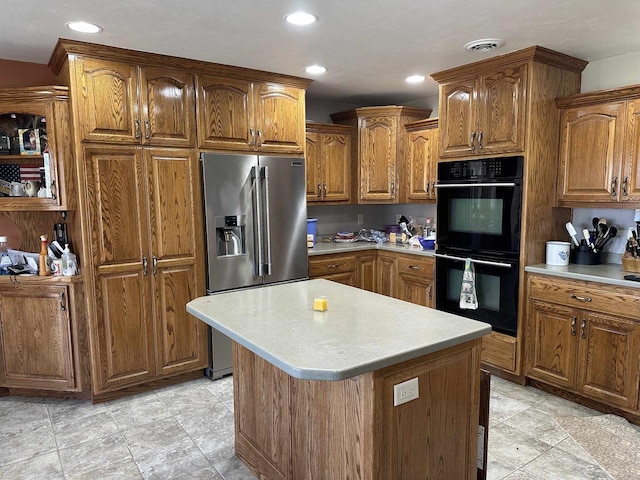 kitchen with brown cabinetry, visible vents, stainless steel fridge, dobule oven black, and light countertops