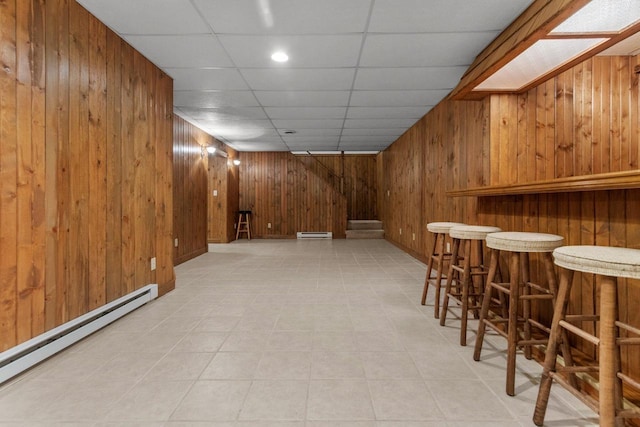 bar with a drop ceiling, wooden walls, and a baseboard radiator