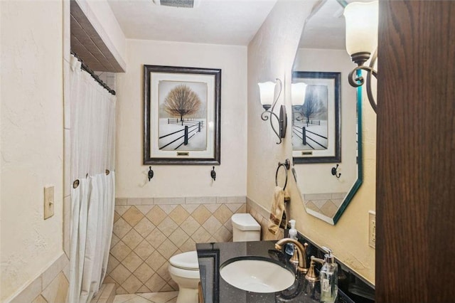 full bath with toilet, a wainscoted wall, tile patterned floors, tile walls, and vanity