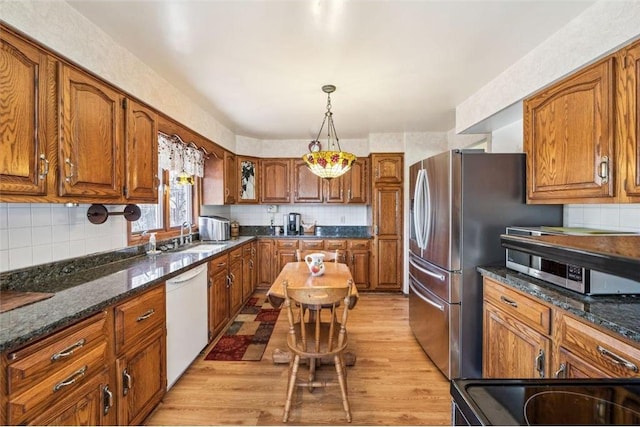 kitchen with brown cabinets, a sink, stainless steel appliances, light wood-style floors, and decorative backsplash