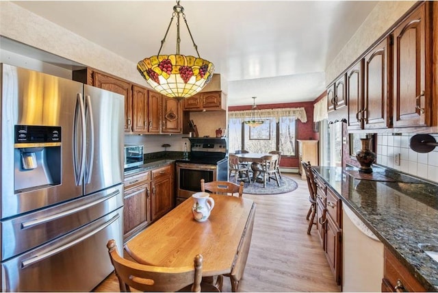 kitchen featuring dark stone counters, light wood-type flooring, decorative light fixtures, appliances with stainless steel finishes, and decorative backsplash