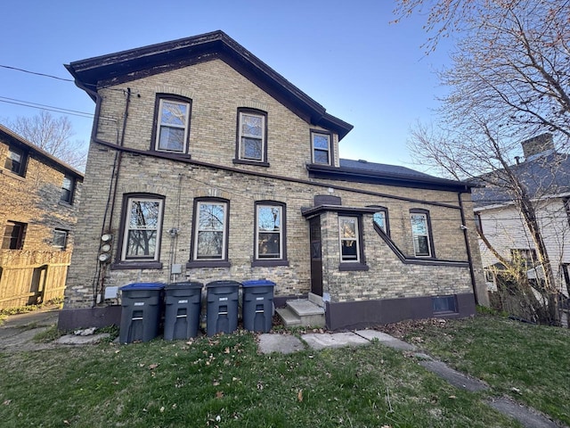 rear view of house featuring brick siding, a yard, and fence