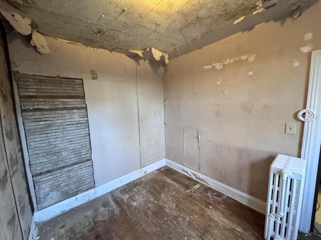 empty room featuring wood finished floors, baseboards, and radiator heating unit
