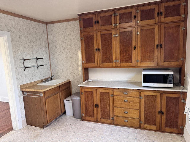 kitchen featuring a sink, brown cabinetry, white microwave, light countertops, and wallpapered walls