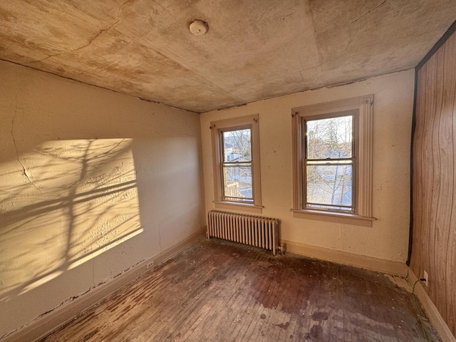 unfurnished room featuring baseboards, hardwood / wood-style floors, and radiator heating unit