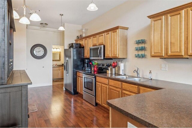 kitchen with decorative light fixtures, dark wood-style flooring, a sink, dark countertops, and appliances with stainless steel finishes