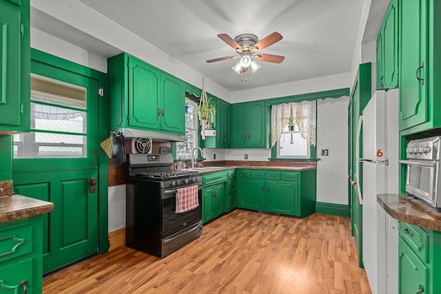kitchen featuring a sink, a ceiling fan, green cabinets, stainless steel gas range, and light wood-style floors