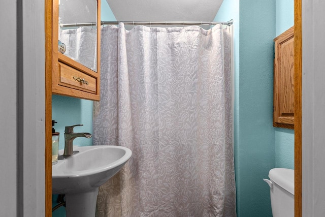full bath with a sink, toilet, a textured wall, and a shower with curtain