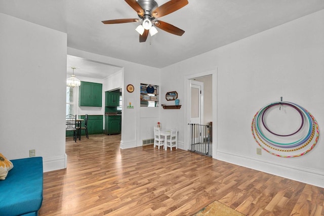 sitting room featuring baseboards, light wood finished floors, visible vents, ceiling fan with notable chandelier, and an upstairs landing
