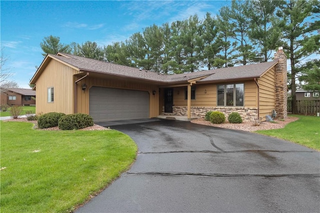 ranch-style home featuring stone siding, a garage, a chimney, a front lawn, and driveway