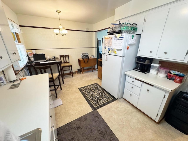 kitchen with freestanding refrigerator, light floors, an inviting chandelier, light countertops, and white cabinets