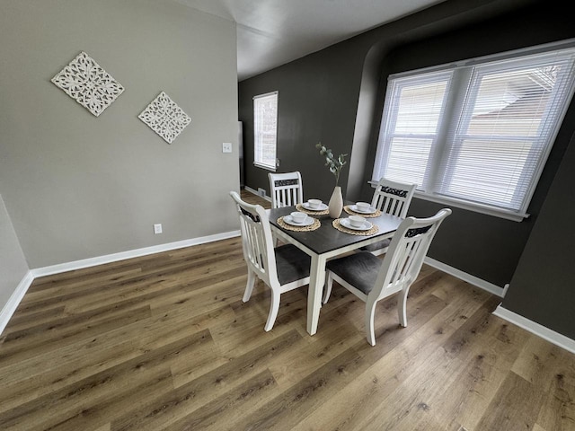 dining space with baseboards, arched walkways, and wood finished floors