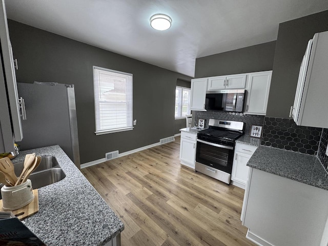 kitchen featuring stainless steel appliances, white cabinets, visible vents, and tasteful backsplash