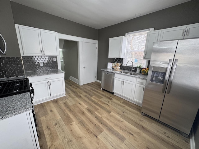 kitchen featuring a sink, backsplash, white cabinets, light stone countertops, and appliances with stainless steel finishes
