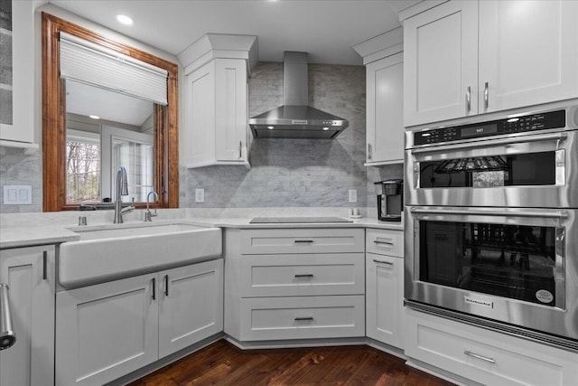 1430 Park Ave, West Bend, WI 53090 - kitchen with wall chimney exhaust hood, stainless steel double oven, a sink, black electric cooktop, and decorative backsplash