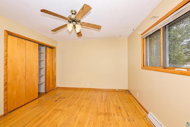 7113 E County Rd E, South Range, WI 54874 - unfurnished bedroom featuring light wood-style floors, a baseboard radiator, baseboards, a textured ceiling, and ceiling fan