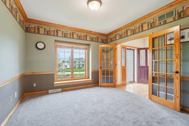 carpeted spare room featuring french doors, a wainscoted wall, ornamental molding, and wallpapered walls