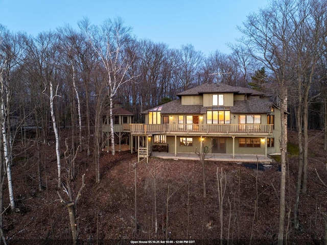rear view of property with a patio area, a wooden deck, a shingled roof, and view of scattered trees