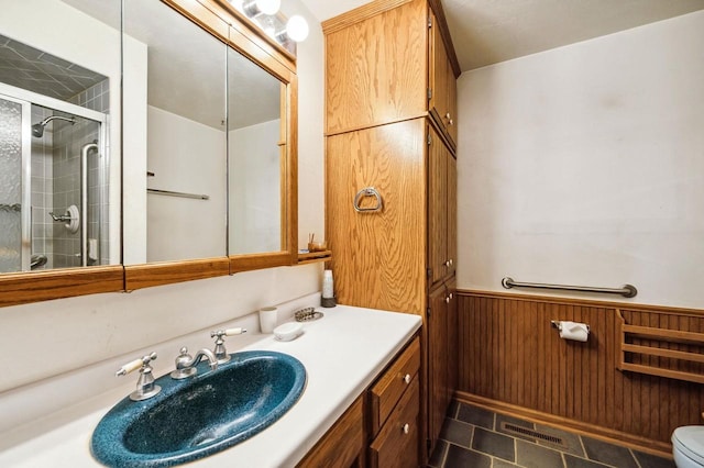 bathroom with a stall shower, vanity, a wainscoted wall, and toilet