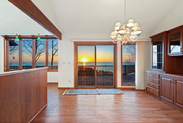 unfurnished dining area featuring vaulted ceiling, a chandelier, wood-type flooring, and baseboards
