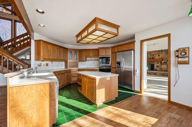 kitchen with stainless steel fridge with ice dispenser, a sink, light countertops, tasteful backsplash, and a center island