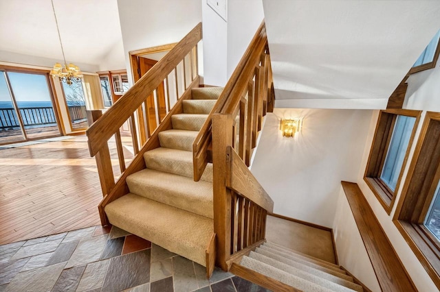 staircase featuring a chandelier, vaulted ceiling, and a water view