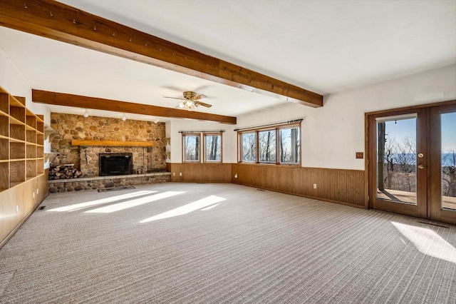 unfurnished living room featuring wainscoting, beam ceiling, wood walls, a fireplace, and carpet floors