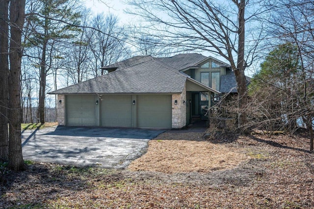 view of side of home with roof with shingles, a garage, driveway, and stone siding