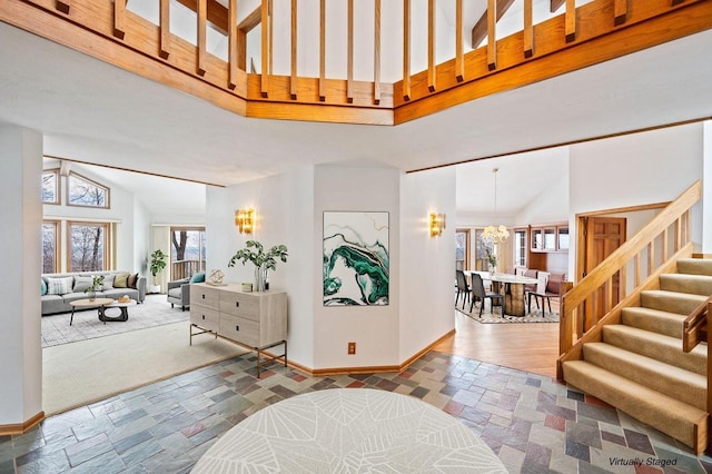 foyer featuring high vaulted ceiling, baseboards, stairs, stone finish floors, and a chandelier