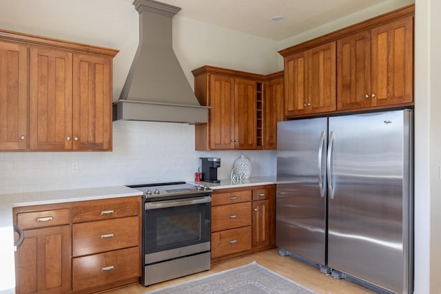 kitchen featuring appliances with stainless steel finishes, custom range hood, brown cabinets, backsplash, and light countertops