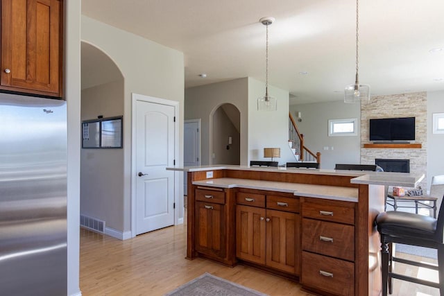 kitchen featuring stainless steel fridge, light wood finished floors, brown cabinets, and arched walkways