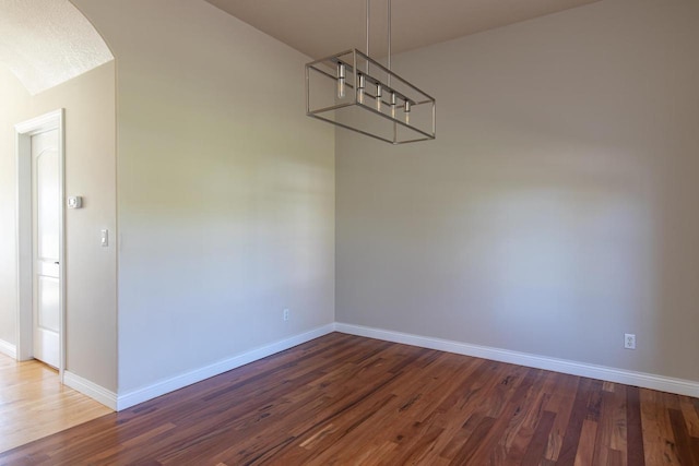 unfurnished dining area featuring wood finished floors, baseboards, arched walkways, and a chandelier