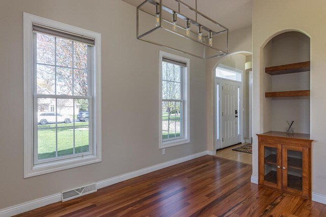 foyer featuring arched walkways, wood finished floors, and baseboards