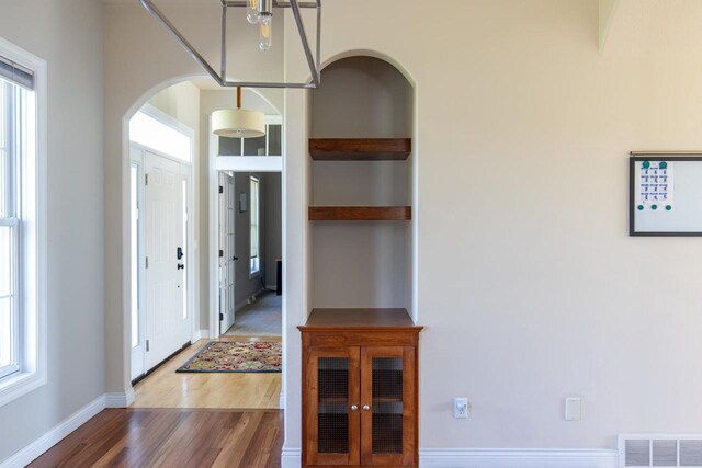entrance foyer featuring wood finished floors, arched walkways, plenty of natural light, and baseboards