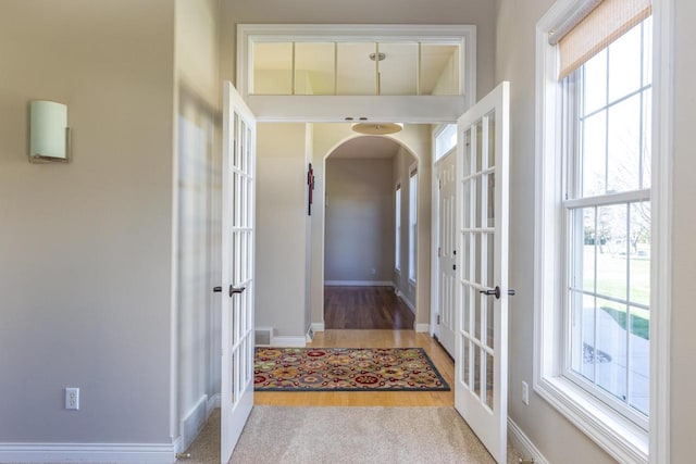 corridor featuring french doors, arched walkways, wood finished floors, and baseboards