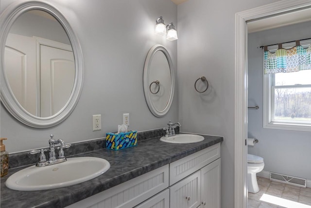 bathroom featuring toilet, double vanity, and baseboards