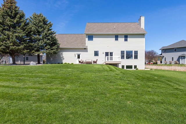 back of property featuring a chimney, a lawn, and roof with shingles