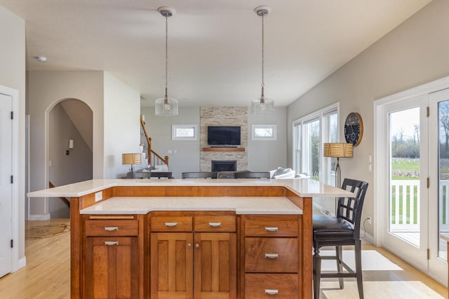 kitchen with light wood finished floors, a fireplace, light countertops, open floor plan, and a kitchen breakfast bar