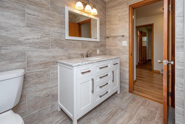 half bathroom with tile walls, toilet, and vanity