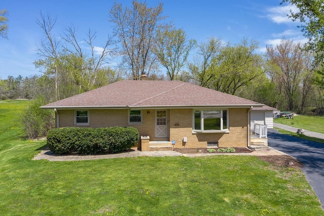 view of front of home featuring brick siding, a front yard, roof with shingles, and a chimney